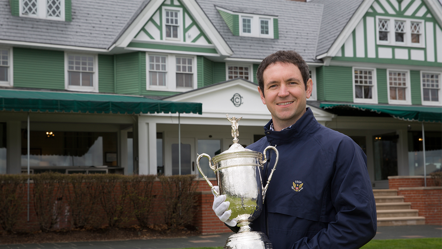 Man standing in front of golf clubhouse while holding trophy