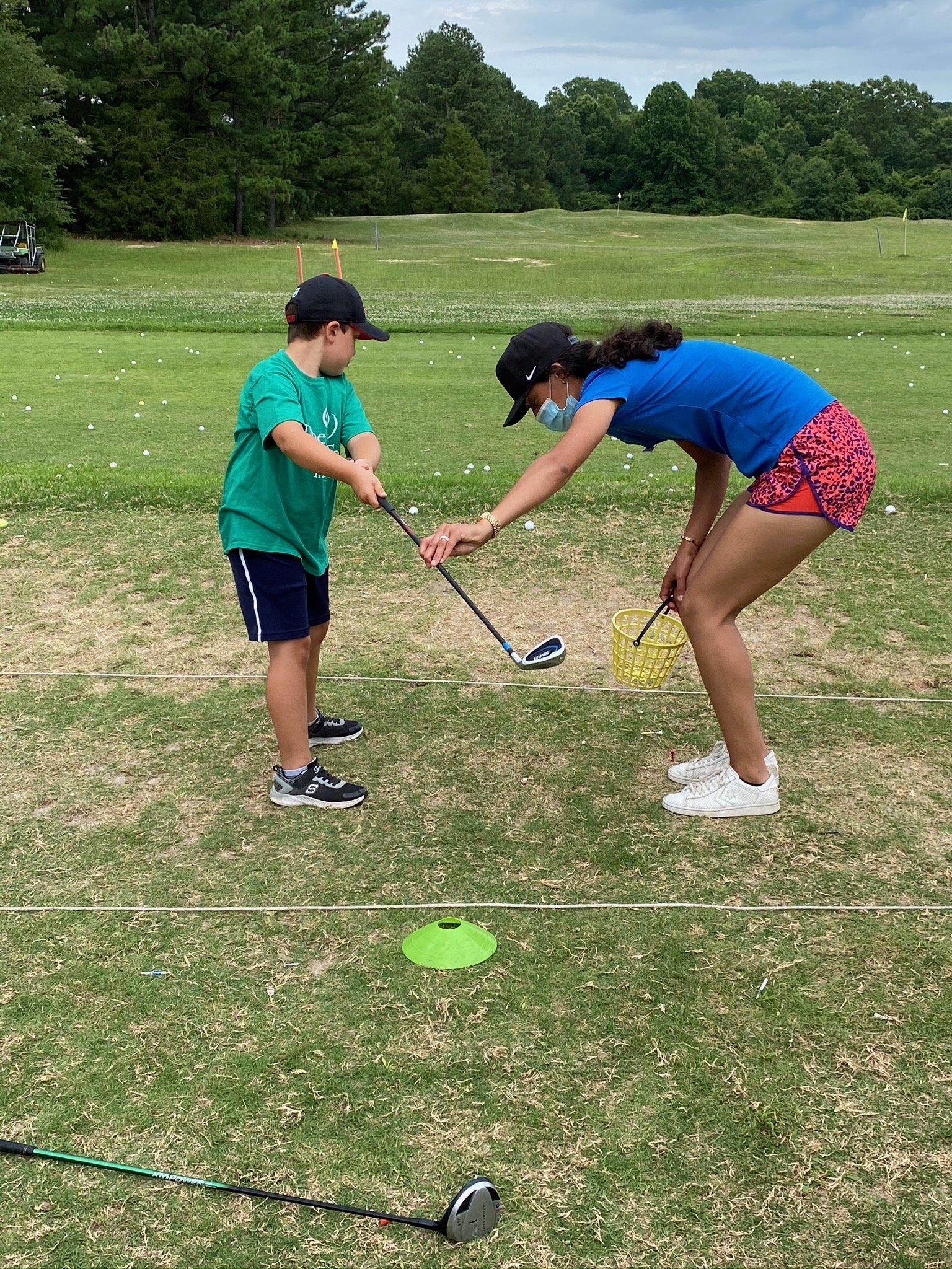 A young woman bends down to teach a boy how to swing a golf club